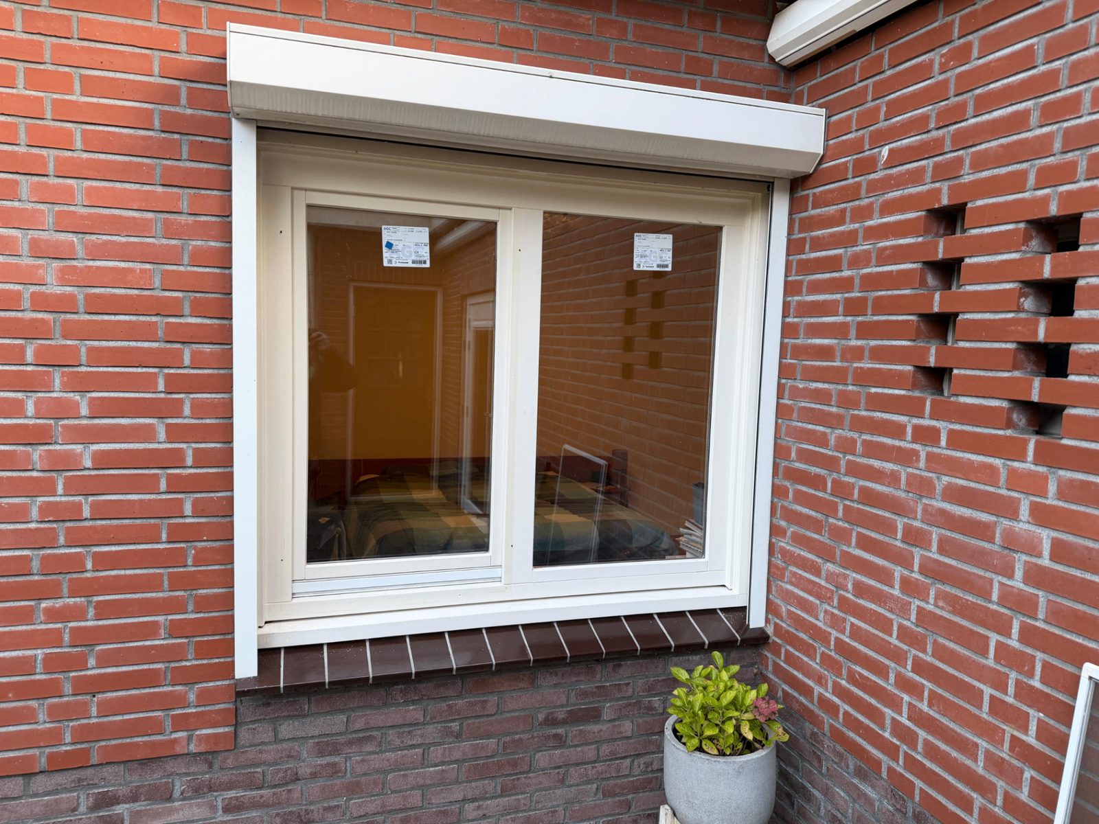 Beglazing in een wit raamkozijn met een bakstenen gevel